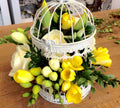 Aranjament de masa in colivie, cu frezii galbene si trandafiri ivoire